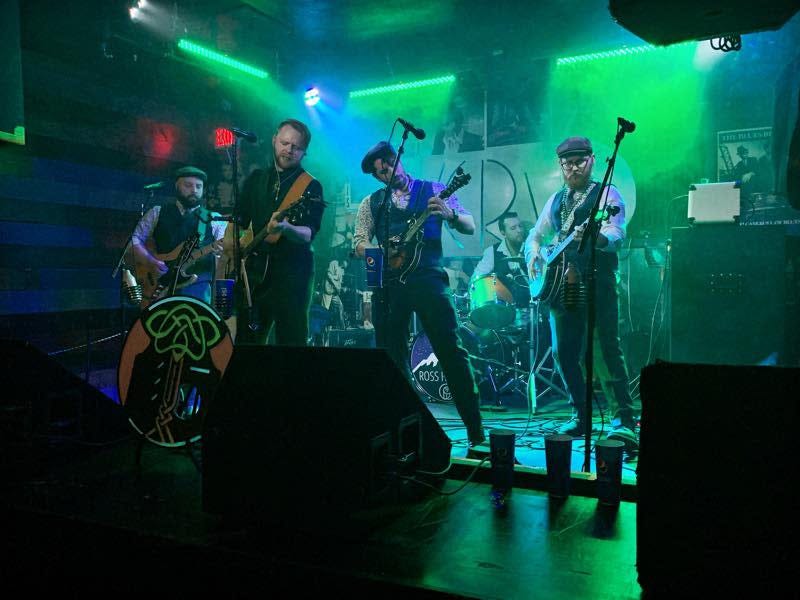 A Celtic rock band performs on a stage. Overlayed on the image of the band are the green and orange of the flag of the Republic of Ireland.